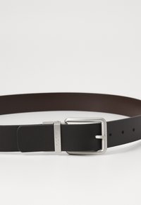 Zwarte en bruine reversible lederen riem met een metalen gesp met merkgravure. De riem heeft meerdere gaatjes voor verstelbare maat.