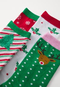 Drei Paar Socken: rot mit weißen Schneeflocken, weiß mit grüner Stechpalme und grün mit einem Rentierdesign und weißen Punkten. Stricktextur.