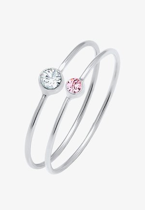 To slanke sølv ringe sammenflettet, med en klar og en lyserød ædelsten ovenpå. Designet er minimalistisk og moderne, med en glat overflade.