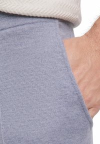 Hellblau gestrickter Stoff der Hose mit sichtbarer Tasche und strukturierten Oberfläche. Nahaufnahme, die das Gewebe und die Form des Materials zeigt.