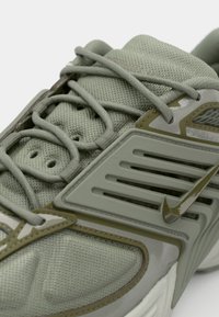 Világos zöld sneaker, texturált hálós felsőrésszel, sima műanyag díszítéssel és kiemelkedő oldalsó panellel, amely szellőzőnyílásokkal és logóval rendelkezik.