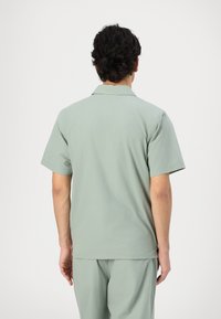 Short-sleeve shirt in light green cotton with a soft texture, featuring a pointed collar and a straight cut, worn with matching pants.