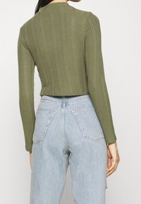 Top de manga larga de canalé verde oliva con un diseño cropped, combinado con unos vaqueros de talle alto azul claro que cuentan con bolsillos traseros y una textura desvaída.