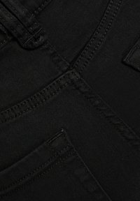 Tissu en denim noir montrant un gros plan des coutures, des joints et d'une poche. Texture lisse avec des variations subtiles dans le tissage.