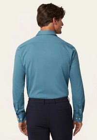 Langemouwige shirt met kraag in teal, gemaakt van een gladde stof. Kenmerkt zich door knoopmanchetten en een rechte achterkant, gecombineerd met donkere broeken.