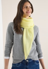 Écharpe jaune en matériau doux, présentant un motif discret en losanges, drapée autour du cou sur un pull gris.