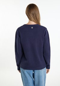 Granatowy sweter dzianinowy z długimi rękawami, okrągłym dekoltem i guzikiem z tyłu. Miękka faktura, luźny krój.