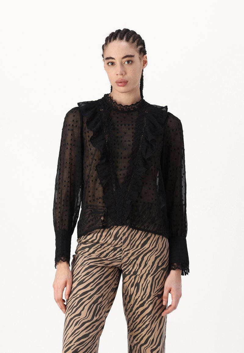 Zwarte doorzichtige blouse met ruches langs de halslijn en voorkant, stippenpatroon en kanten accenten. Gecombineerd met zebra print broeken.