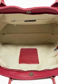 Sac en cuir rouge avec un intérieur beige spacieux, doté d'une poche zippée et d'un petit patch texturé pour un détail supplémentaire.