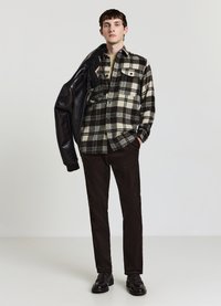 Schwarz-creme kariertes Flanellhemd mit zwei Brusttaschen, braune Cordhosen und eine schwarze Lederjacke, die über einer Schulter liegt.