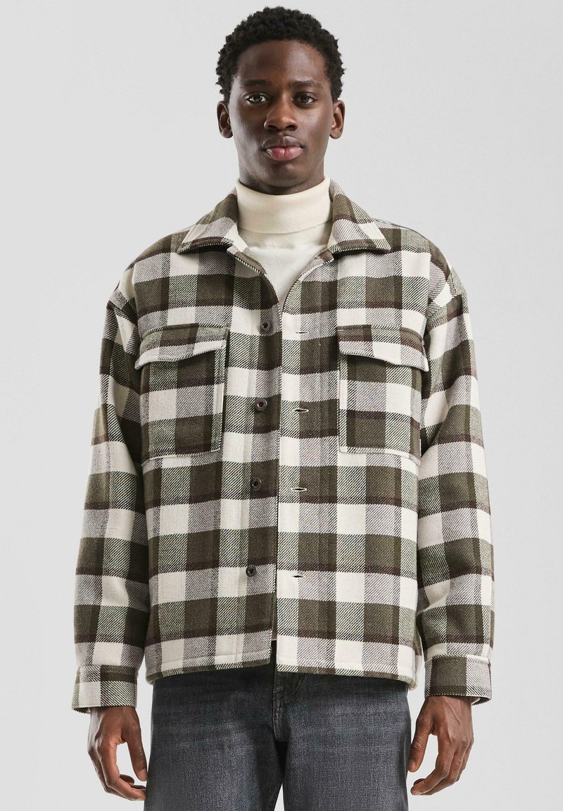 Geruite jas in groen en wit, gemaakt van dikke stof. Voorzien van twee borstzakken, knoopsluiting en een kraag.