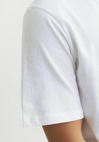 Hvid bomulds t-shirt med rund halsudskæring og korte ærmer. Stoffet har en glat tekstur med dobbeltstikninger i fancyen.