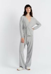 Grijze gebreide loungeoutfit met een wikkeltop met een diepe V-hals en lange mouwen, gecombineerd met wijde broekspijpen. Zachte textuur en casually fit.