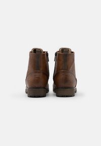 Bottines en cuir marron avec une texture lisse, fermeture à glissière à l'arrière et une semelle en caoutchouc robuste. Présentent des panneaux élastiques latéraux pour un ajustement optimal.