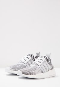 Svartvita stickade träningsskor med strukturerad ovandel, vita snören och en dämpad sula. Har logotypdetaljer och dragflikar.