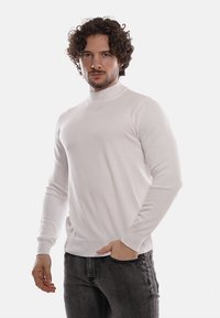 Maglione bianco a collo alto realizzato in tessuto morbido, con polsini e orlo a coste, abbinato a jeans scuri slim-fit.