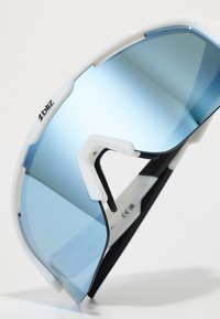 Białe i czarne sportowe okulary przeciwsłoneczne z dużymi, niebieskimi gradientowymi soczewkami, charakteryzujące się eleganckim designem i regulowanymi zausznikami dla wygody.