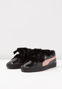 Černé lakované nízké tenisky s širokými černými sametovými tkaničkami a růžovým bočním pruhem na texturovaných černých gumových podrážkách.