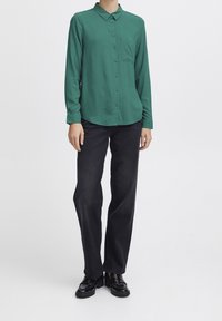 Groene overhemd met lange mouwen, een kraag, een borstzak en een knopen ontwerp. Gecombineerd met zwarte rechte broek en glanzende schoenen.