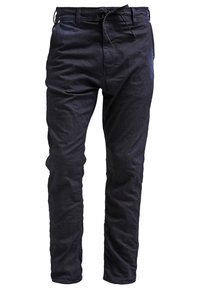 Pantaloni blu scuro in tessuto morbido e strutturato. Presentano una vita con coulisse, una vestibilità slim e dettagli minimi.