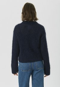 Navy blue knit sweater with a relaxed fit, wide sleeves, and ribbed hem. Made from a fluffy, textured material, styled for comfort.