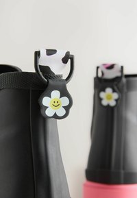 Bottes de pluie en caoutchouc noir avec une finition texturée, ornées de poignées en forme de vache et d'accents en forme de fleur souriante en blanc et jaune.