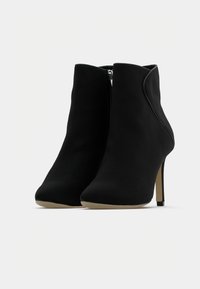 Botines negros de tobillo fabricados con material suave, con punta afilada, tacón de aguja delgado y cremallera lateral con detalles de costura elegantes.