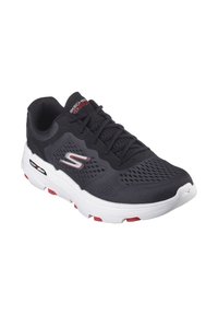 Black athletic shoe with a mesh upper, white and red outsole, textured surface, and flat laces. Features the Skechers logo on the side.