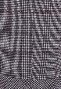 Tissu pied-de-poule noir et blanc présentant un motif à carreaux avec des accents rouges. Texture lisse avec un design vif et contrasté.