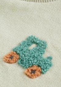 Zelený texturovaný hrací kamion s hnědými koly vyšitý na béžové pletené tkanině.