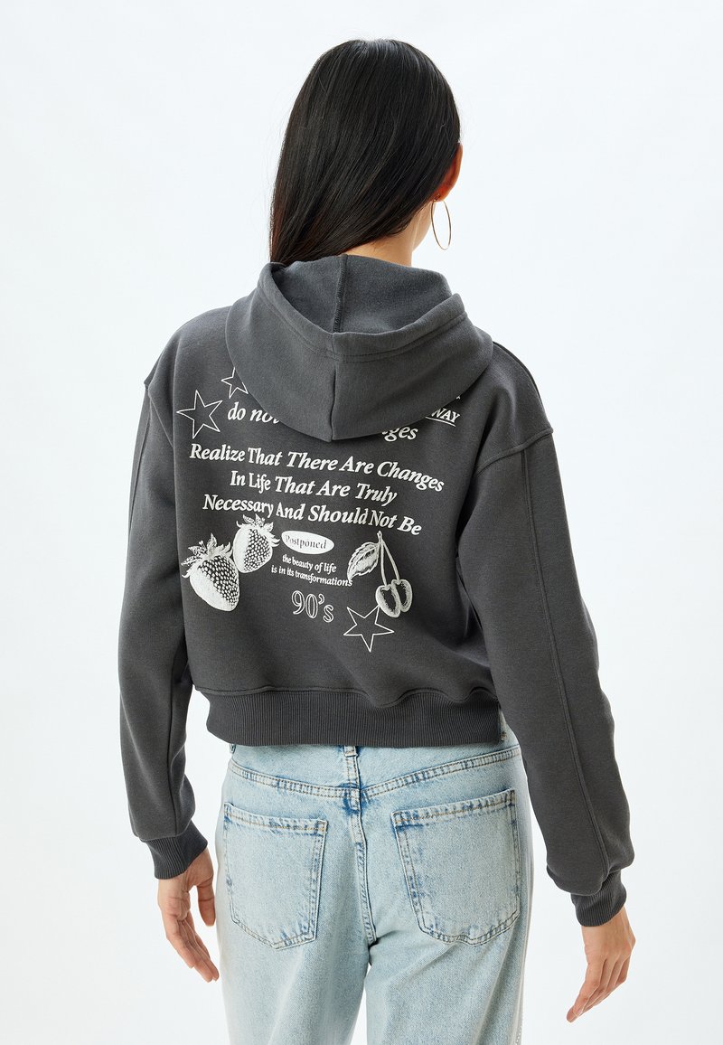 Sudadera corta gris con capucha ajustable. Presenta texto blanco y diseños gráficos que incluyen estrellas, fresas y elementos textuales en la parte posterior.