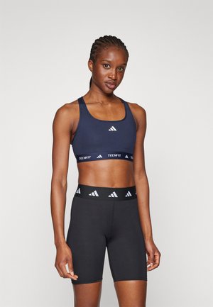 Marine sport crop top met een brede band gelabeld "TECHFIT" en zwarte hoge shorts met een contrasterende logoband in de taille.