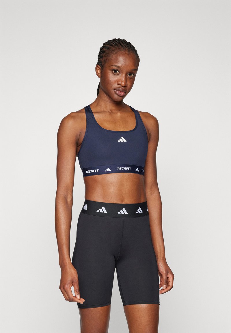 Marine sport crop top met een brede band gelabeld "TECHFIT" en zwarte hoge shorts met een contrasterende logoband in de taille.