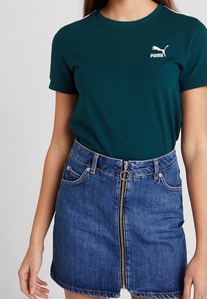 Zielona bawełniana koszulka z krótkim rękawem i białym logo Pumy, w połączeniu z niebieską dżinsową spódniczką mini z zamkiem błyskawicznym z przodu i kieszeniami.