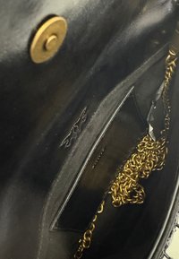 Interno di una borsa in pelle nera con una tracolla in catena dorata, tasca interna nera e chiusura magnetica in ottone.