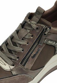 Brun syntetisk sneaker med mesh-accenter, texturerad yta, snörning och sidodetalj med dragkedja. Har en gummisula och logotypprydnad.