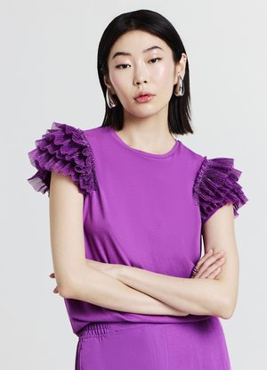 Haut violet à manches courtes avec des volants texturés sur les épaules. Tissu lisse avec un col rond et une coupe décontractée.