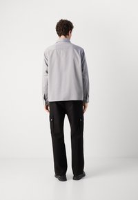 Light gray long-sleeve shirt with a collar, paired with black cargo pants featuring side pockets. Smooth texture, practical design.