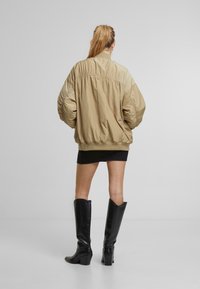 Kaki bomber-jakk lõdva lõikega, õlgadele kogutud detailid ja ribatud äär, kantud musta mini-seeliku ja põlve kõrguste saapadega.