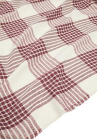 Tessuto intrecciato rosso e crema con un motivo a scacchi, strisce e bordi frangiati. Il materiale appare testurizzato e morbido.