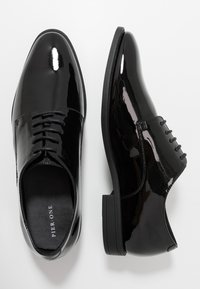 Chaussures de cérémonie en cuir verni noir avec une finition lisse, bout rond et fermeture à lacets à six œillets. Semelle en caoutchouc avec un profil minimal.
