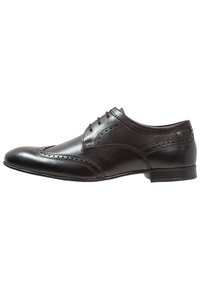 Chaussure brogue en cuir noir avec un bout arrondi, des perforations détaillées et six œillets pour les lacets. Texture lisse, talon empilé bas.