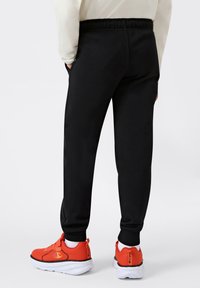 Zwarte sweatpants met een elastische tailleband, zijzakken en taps toelopende benen, gecombineerd met fel oranje sportschoenen met een mesh-textuur.