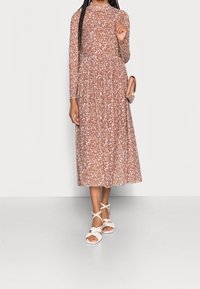 Brun blommig midikjol med långa ärmar, draperad midja och en svängd kjol. Matchad med vita snörskor och en rosa axelväska.