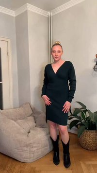 Mørkegrønn, langermet kjole med V-hals, sidespalte og ribbet tekstur; kombinert med svarte knelange støvler og satt mot en lys bakgrunn.