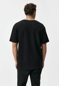 Czarny, krótki rękaw, t-shirt wykonany z teksturowanej tkaniny o luźnym kroju. Okrągły dekolt, gładki wzór.