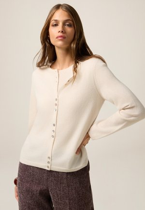 Cárdigan beige claro hecho de tela suave, con cuello redondo, mangas largas y botones decorativos en el frente.