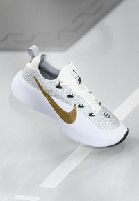White and gray patterned Nike sneaker with thick sole and metallic gold swoosh, shown on a light gray surface.