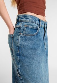 Modré džíny z denimu s vysokým pasem, pěti kapsami a oranžovým prošitím. Tkanina má vybledlou texturu s mírným opotřebením.