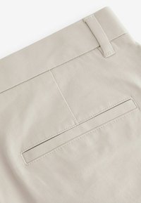 Beige pamut szövet sima felülettel, hátsó zsebbel és letisztult varrással a széleken. Egyszerű, funkcionális dizájn.